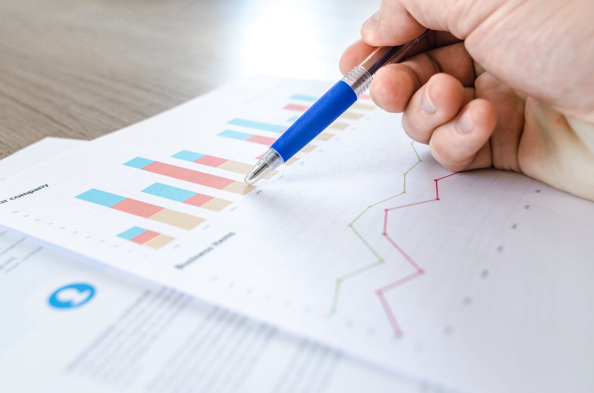 Hand pointing with blue pen at printed business charts and graphs on a desk